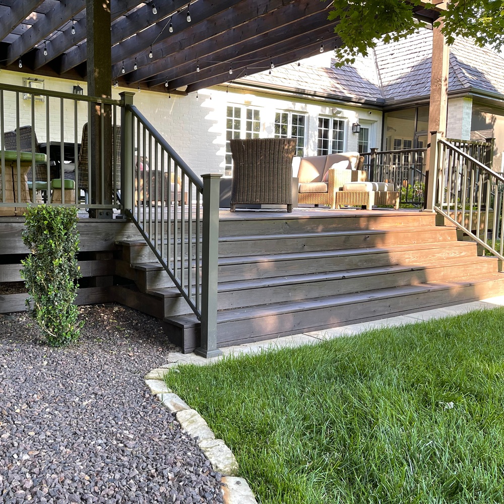 Fresh stain being applied to a backyard deck beside an occupied home